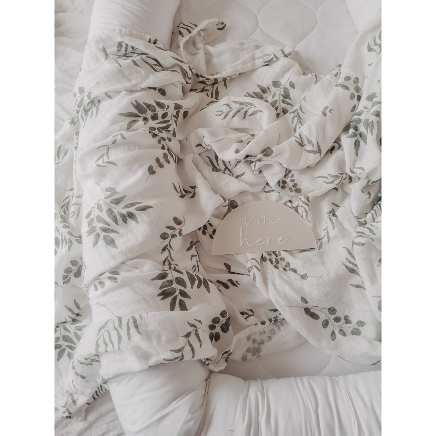 Remy&Co Muslin Wrap in Eucalyptus design. Baby swaddle wrap layed over baby bed